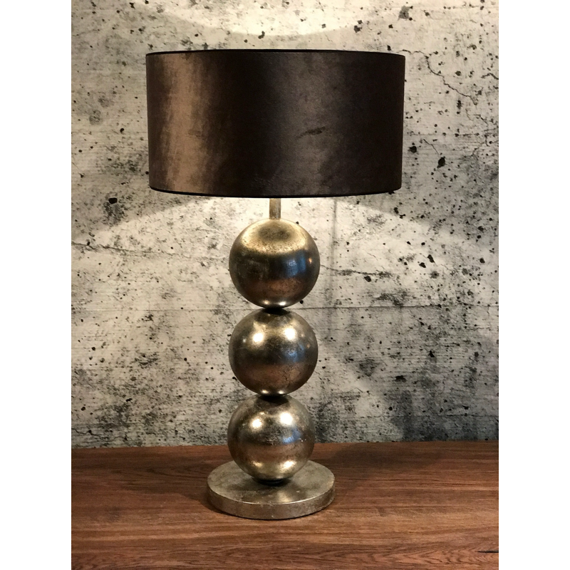 Tafellamp met drie metalen bollen en een donkere kap, op een houten tafel.