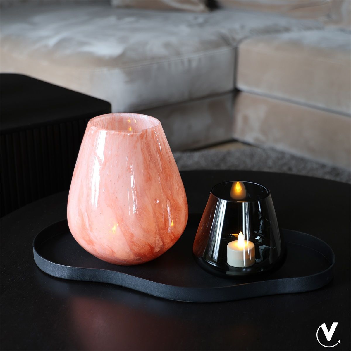 Roze decoratieve diffuser en zwarte kaarsenhouder op een zwart dienblad in een woonkamer.