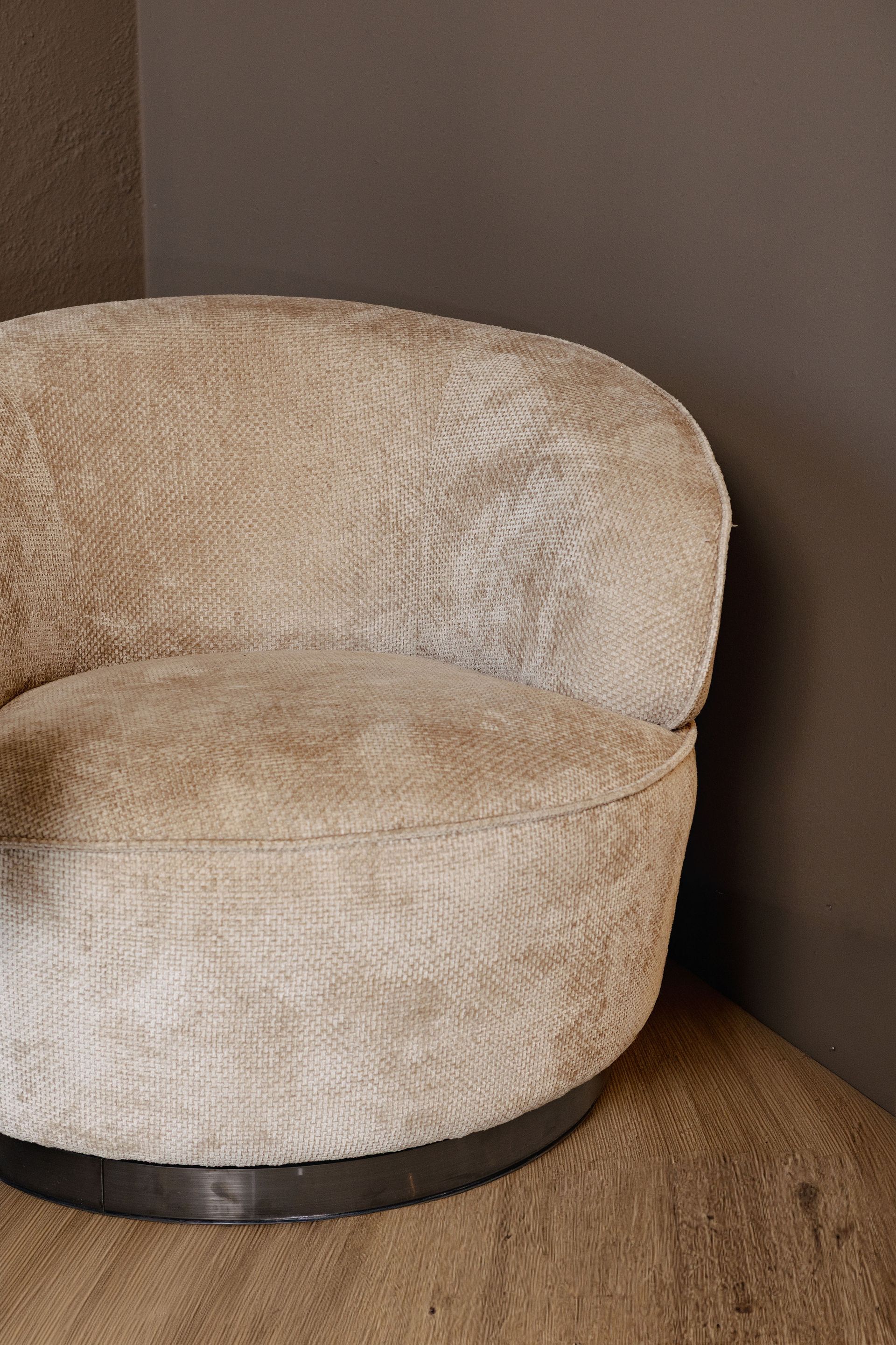 Beige ronde fauteuil met gestructureerde bekleding in een hoek naast een bruine muur.
