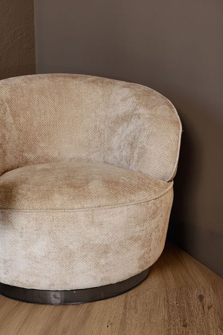 Beige ronde fauteuil met structuurstof in een hoek op een geweven vloerkleed.