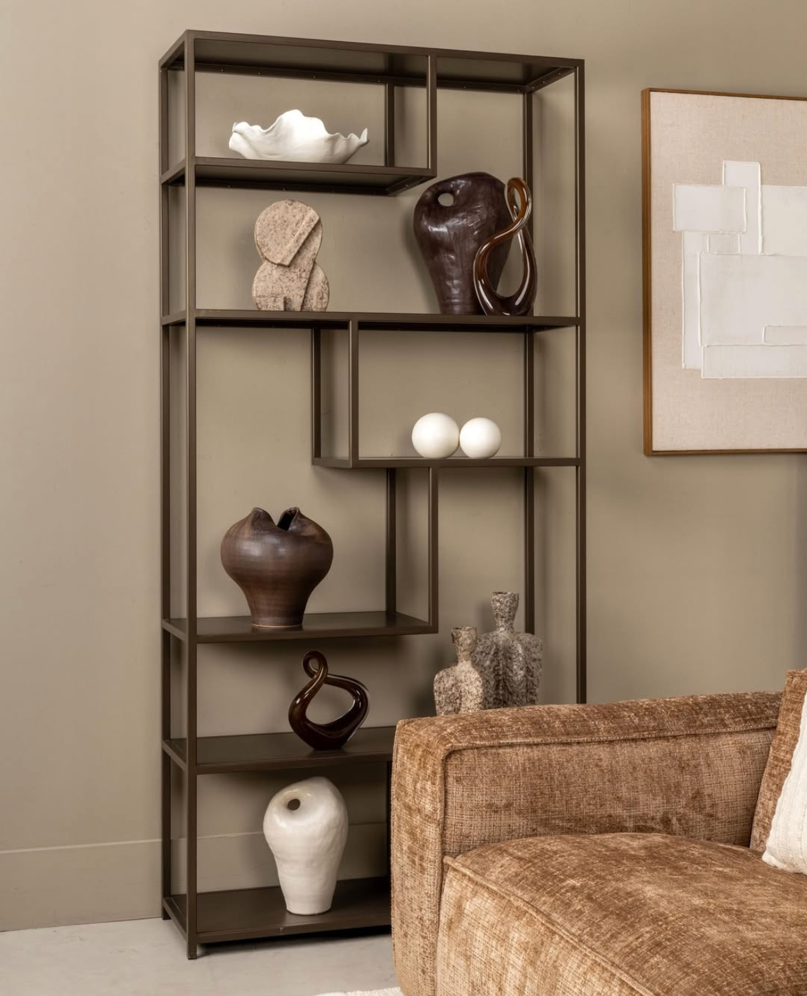 Moderne woonkamer met donkere planken waarop sculpturen en decoraties staan, naast een beige bank.