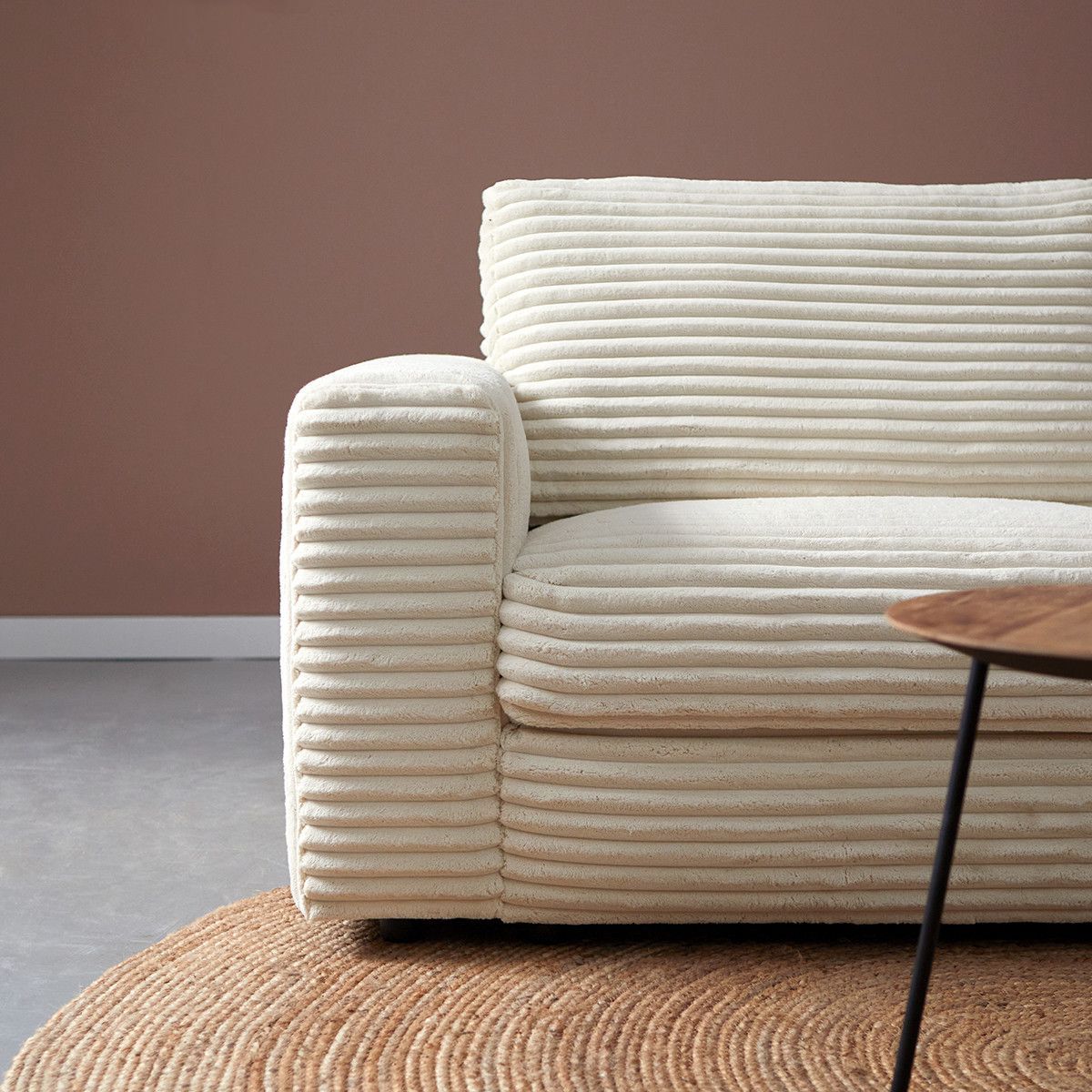 Moderne beige gestreepte hoekbank met salontafels op een rond vloerkleed tegen een bruine muur.