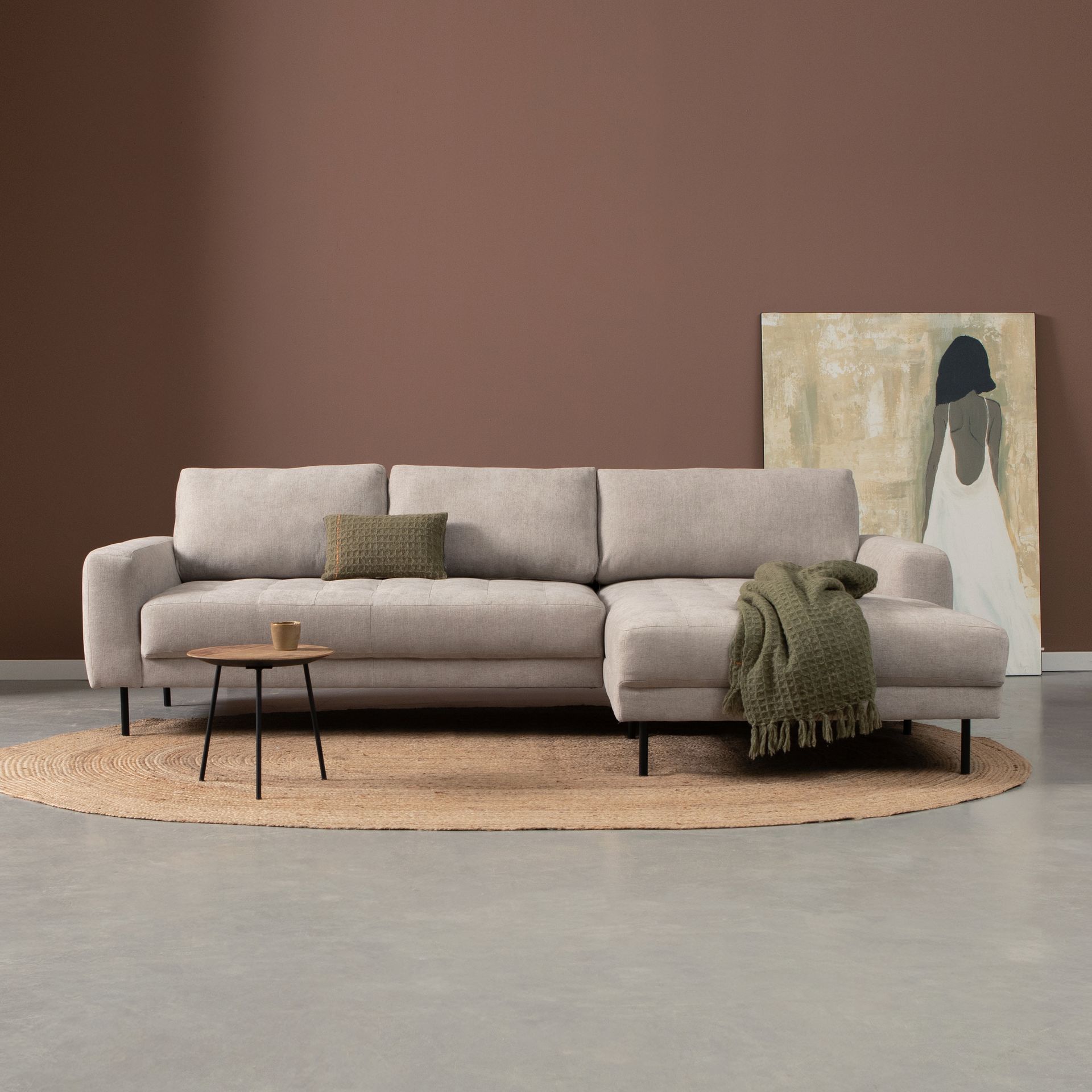 Een minimalistische beige bank op een rond vloerkleed met een klein tafeltje en abstracte muurdecoratie.