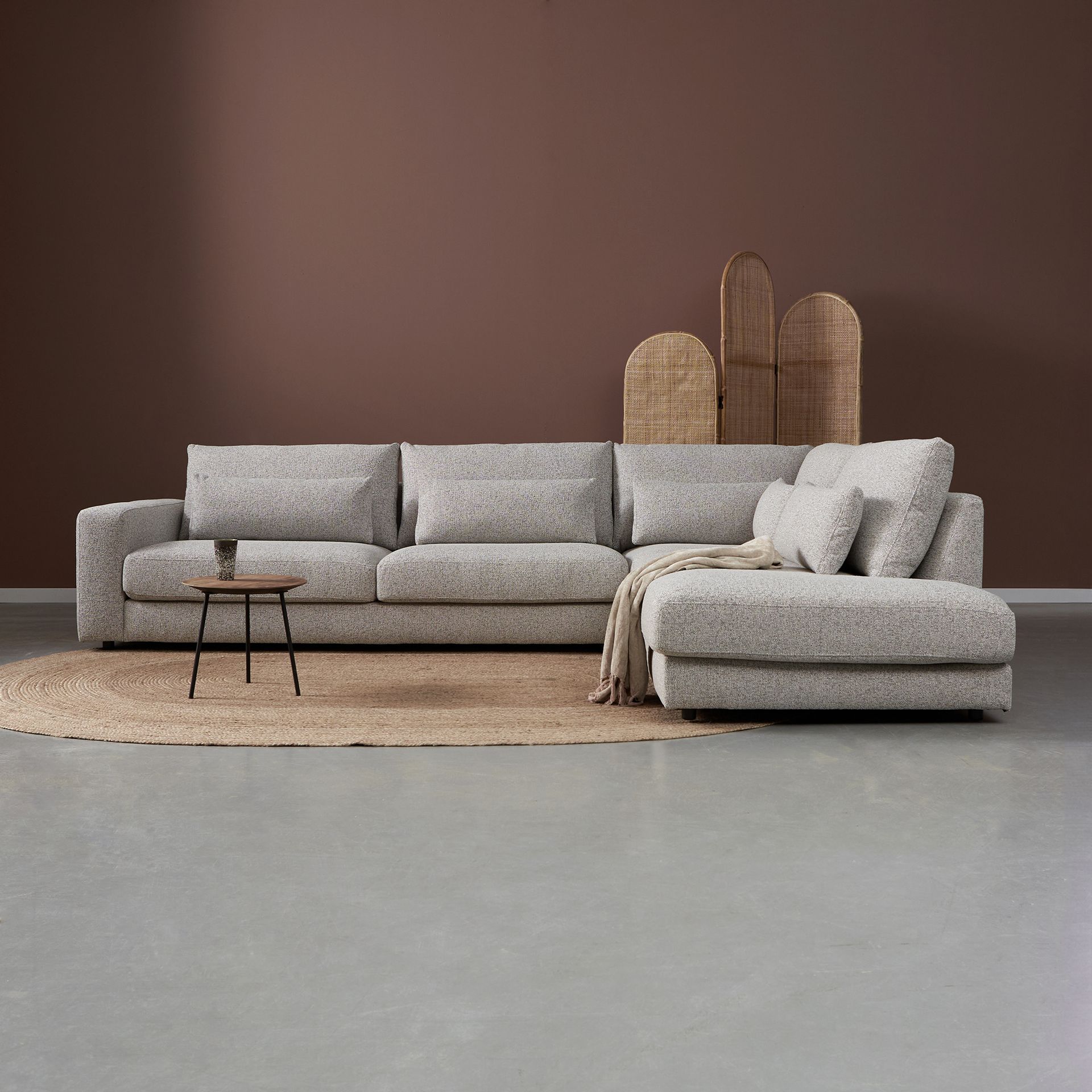 Grijze hoekbank met kussens en salontafel op een vloerkleed in een minimalistische woonkamer.