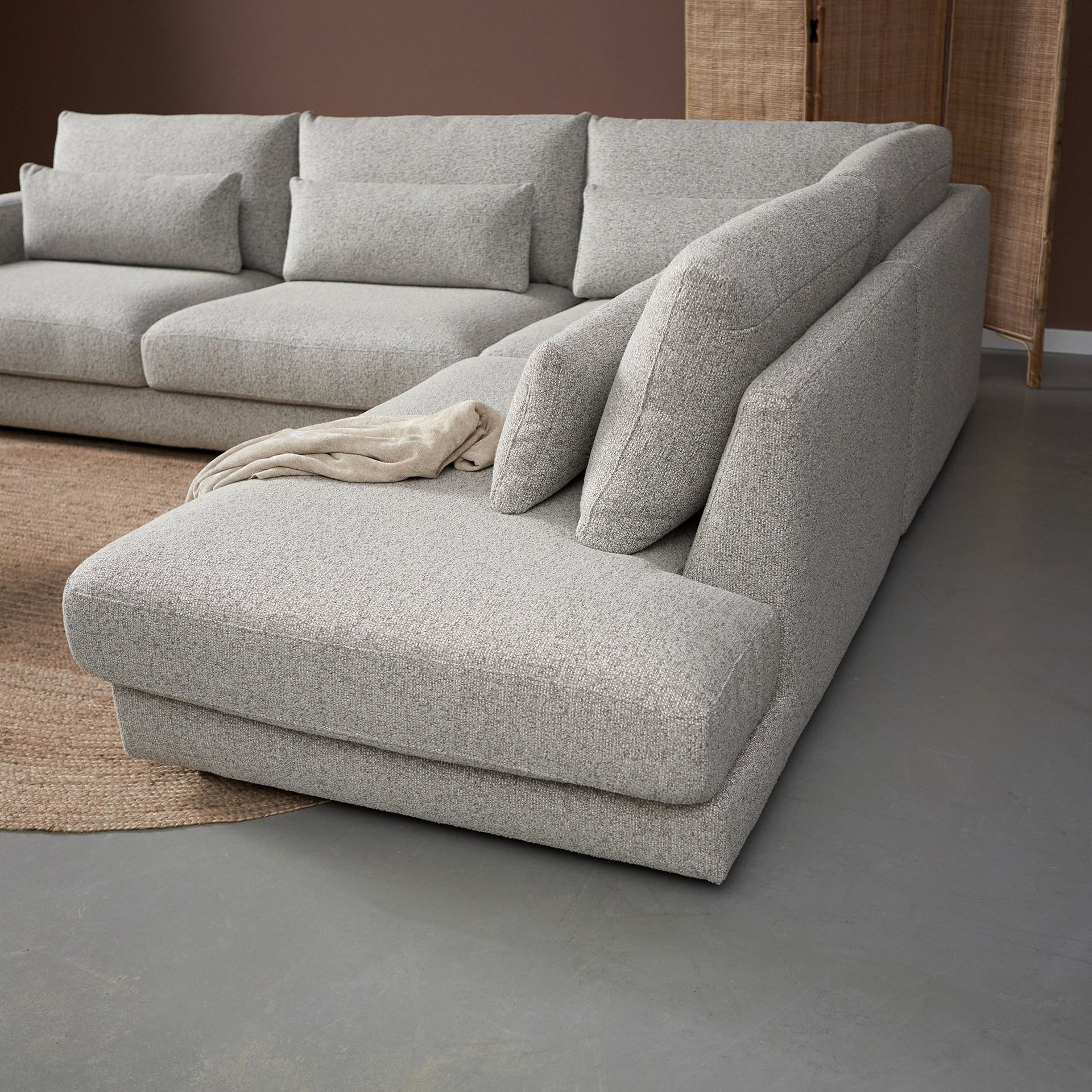 Grijze hoekbank met kussens en salontafel op een vloerkleed in een minimalistische woonkamer.