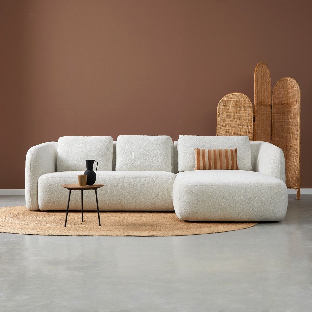 Minimalistische woonkamer met een witte bank en poef, een klein tafeltje, een geweven kamerscherm.