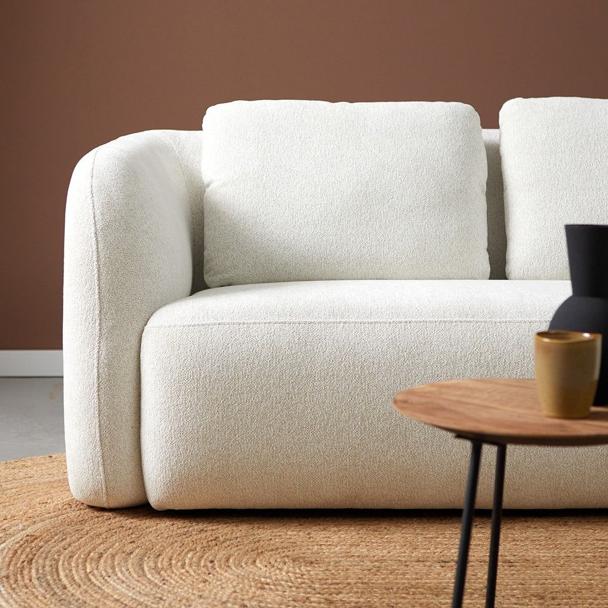 Minimalistische woonkamer met een witte bank en poef, een klein tafeltje, een geweven kamerscherm.