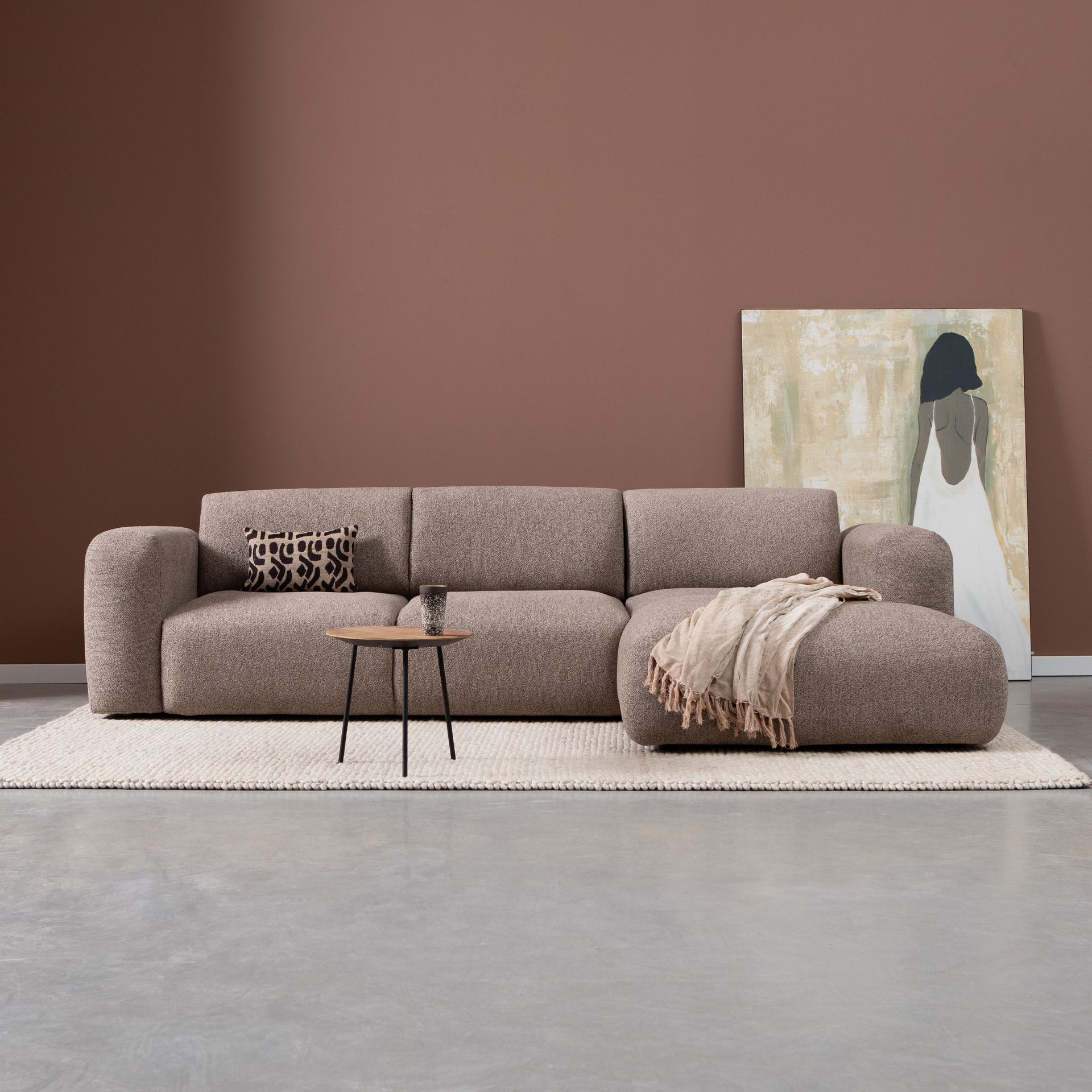Minimalistische woonkamer met een taupekleurige hoekbank, een kussen met patroon, een bijzettafel.