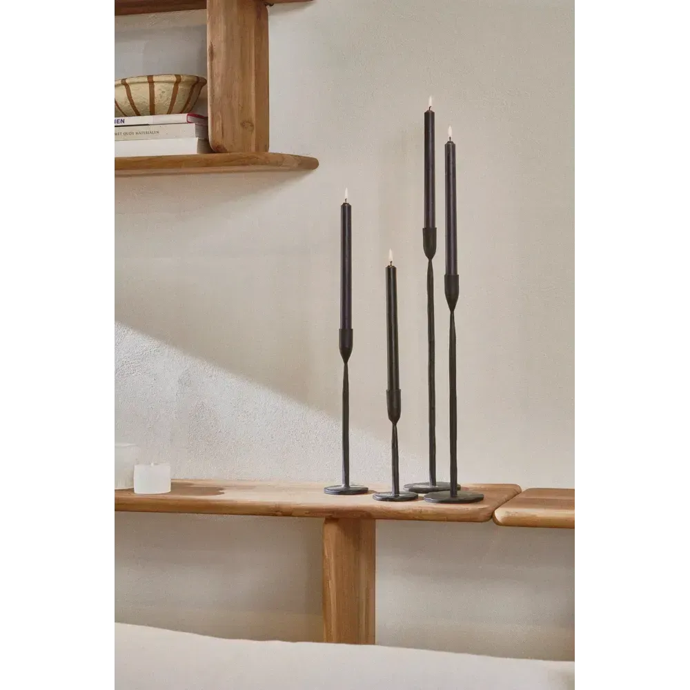 Vier zwarte kandelaren van pomax met zwarte kaarsen op een houten plank tegen een lichte muur.