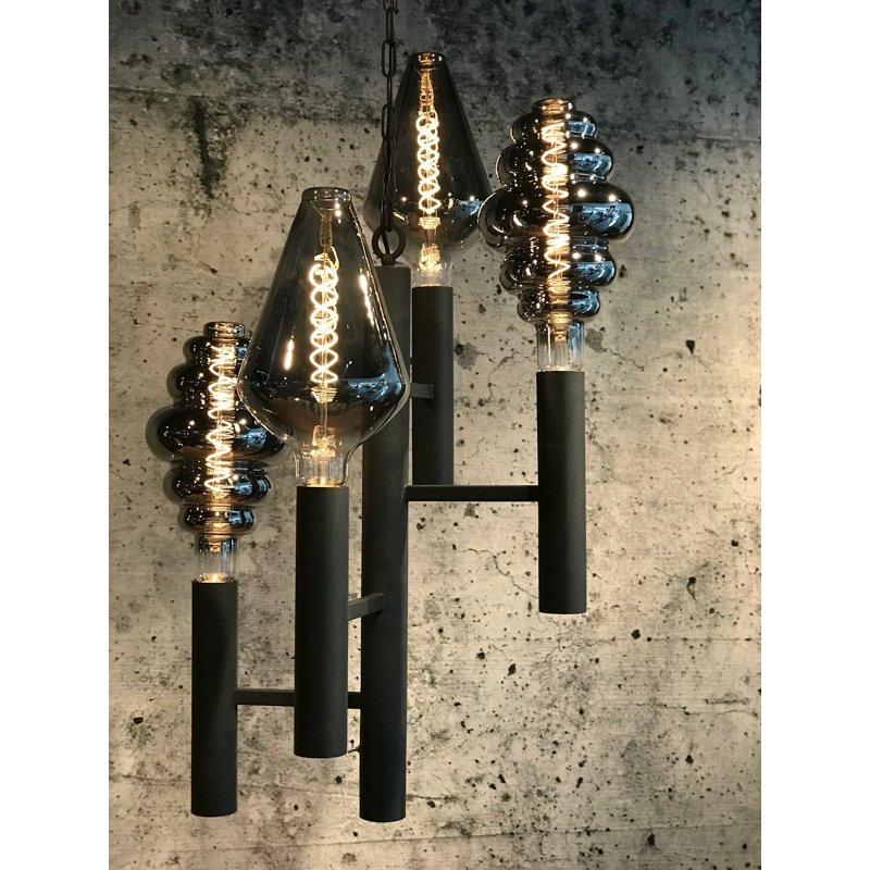 Zwarte kroonluchter met vier donkergetinte lampen, tegen een grijze betonnen muur met structuur.