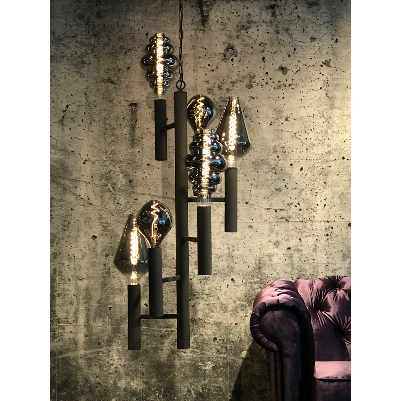 Een zwarte kroonluchter met decoratieve lampen tegen een muur van gestructureerd beton, naast een paarse bank.