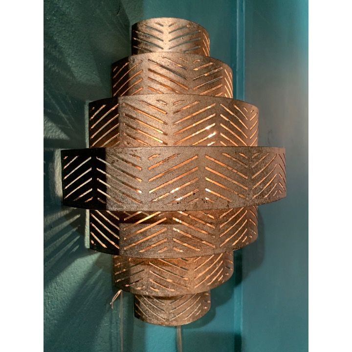 Bronzen, gelaagde wandlamp met een geometrisch patroon, die warm licht uitstraalt.