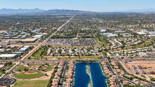 Aerial view of a suburban neighborhood with blue water features, a baseball field, and a long road under a clear sky.