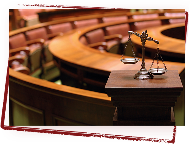 A scale of justice on a wooden table in a courtroom, representing Todaro David M Co LPA, a personal injury attorney in Canton, OH. Scales of justice on a wooden stand in a courtroom with curved wooden seating.