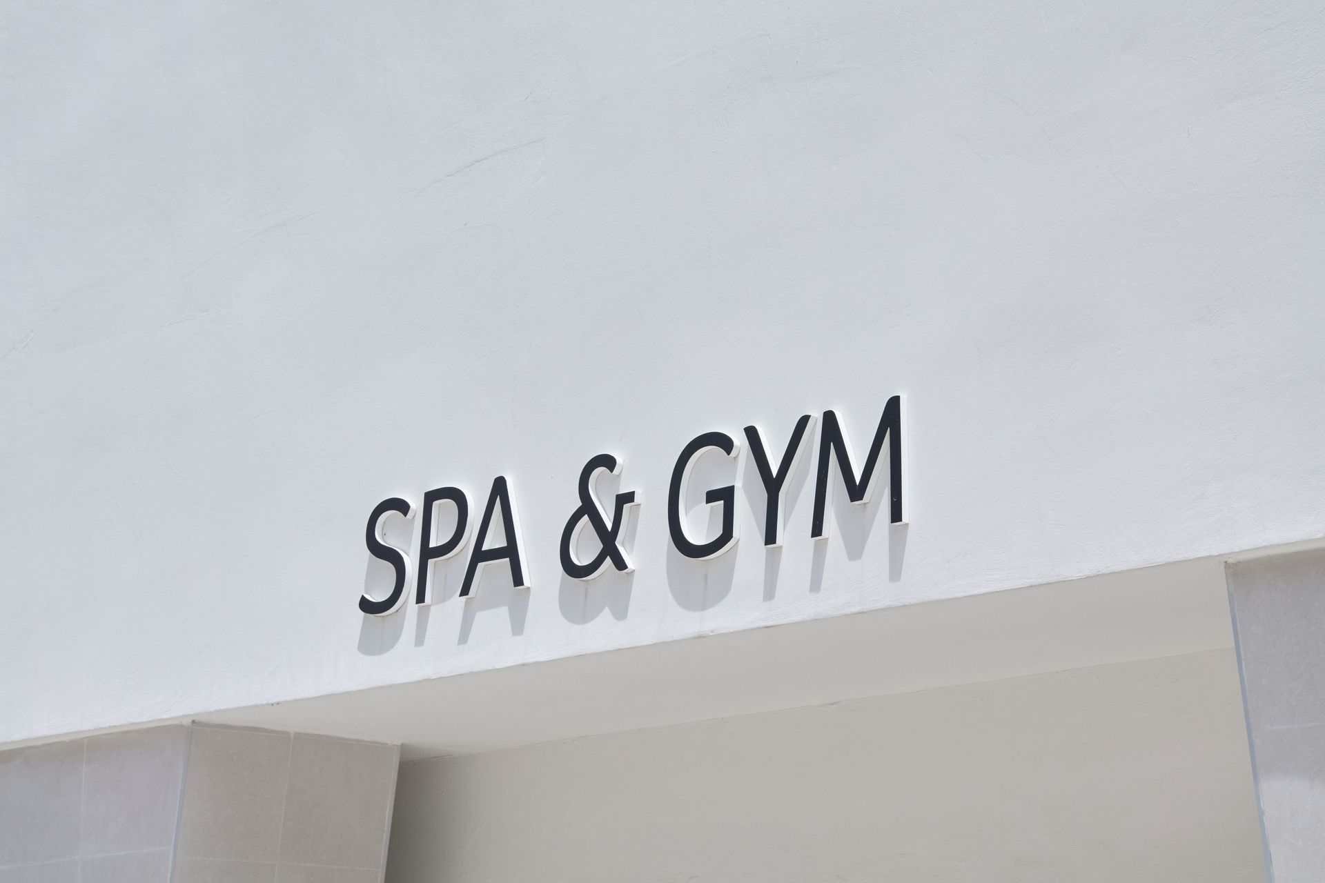 Black dimensional letters spelling SPA & GYM mounted on a white exterior wall