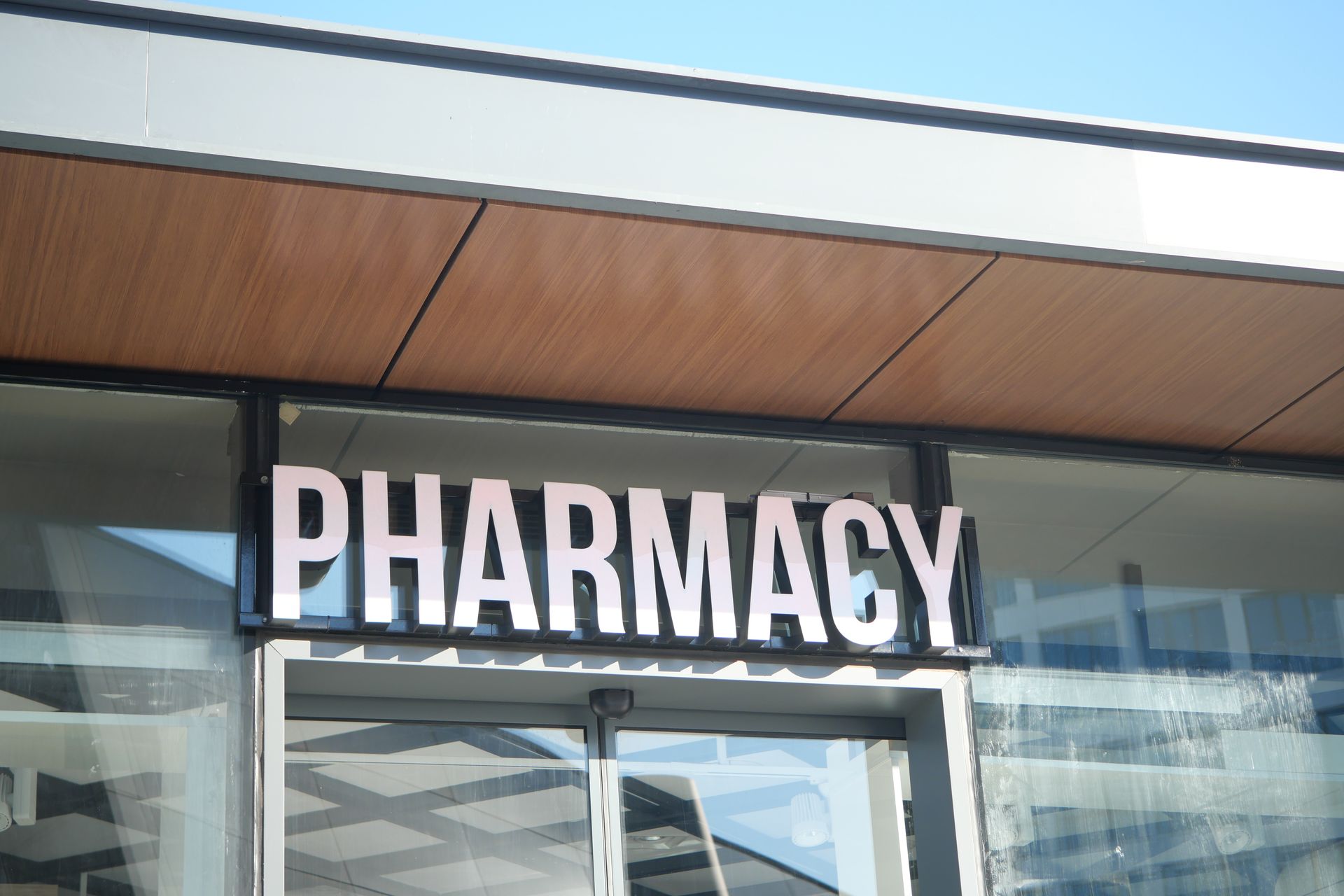 Pharmacy storefront with large white “PHARMACY” sign above glass doors.