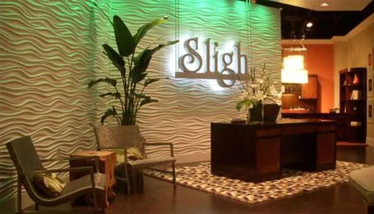 Modern lobby with a reception desk, illuminated “Sligh” sign, potted plants, and patterned wall decor