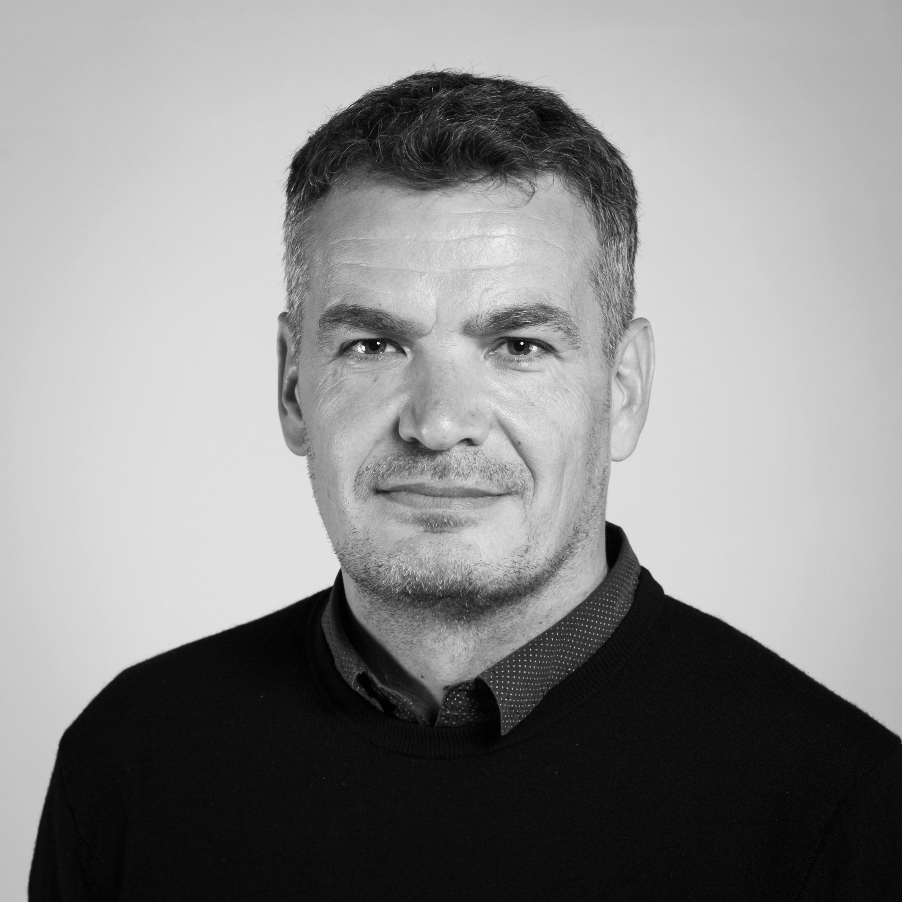 Une photo en noir et blanc d'un homme portant un pull noir et une chemise.
