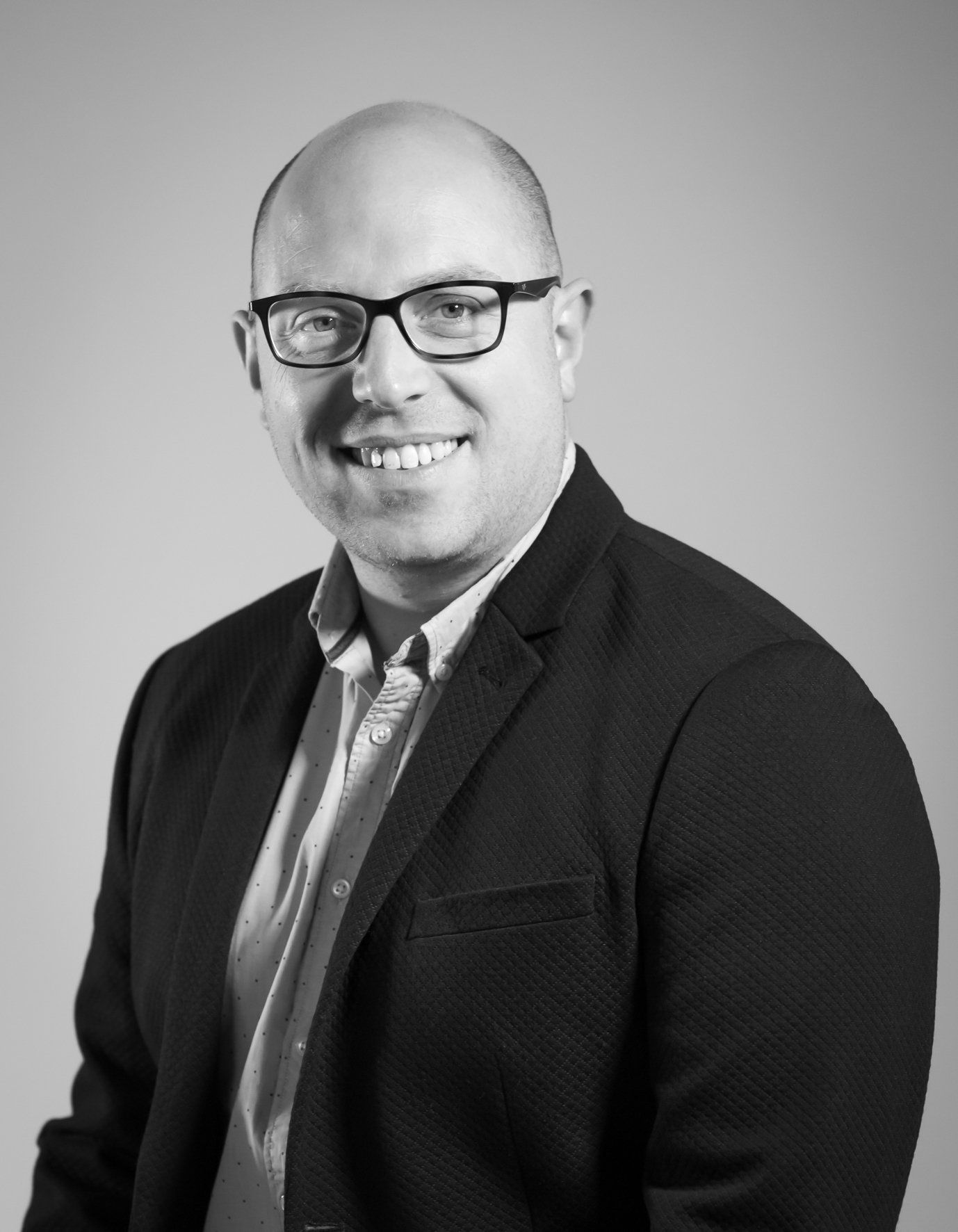 Un homme portant des lunettes et un costume sourit sur une photo en noir et blanc.