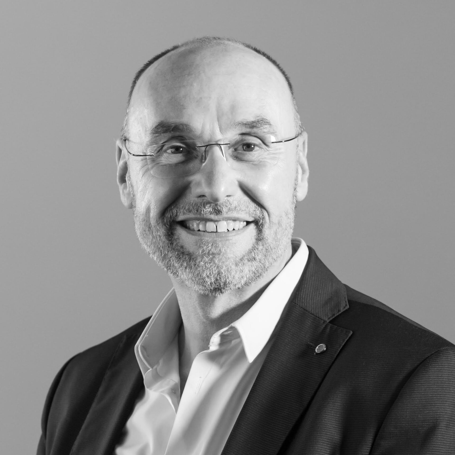 Un homme en costume et lunettes sourit sur une photo en noir et blanc.