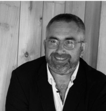 Un homme avec une barbe et des lunettes sourit sur une photo en noir et blanc.