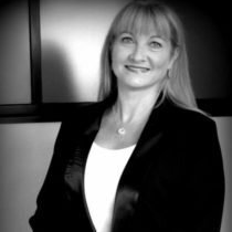 Une femme portant une veste noire et une chemise blanche sourit sur une photo en noir et blanc.