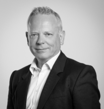 Un homme en costume et chemise blanche sourit sur une photo en noir et blanc.