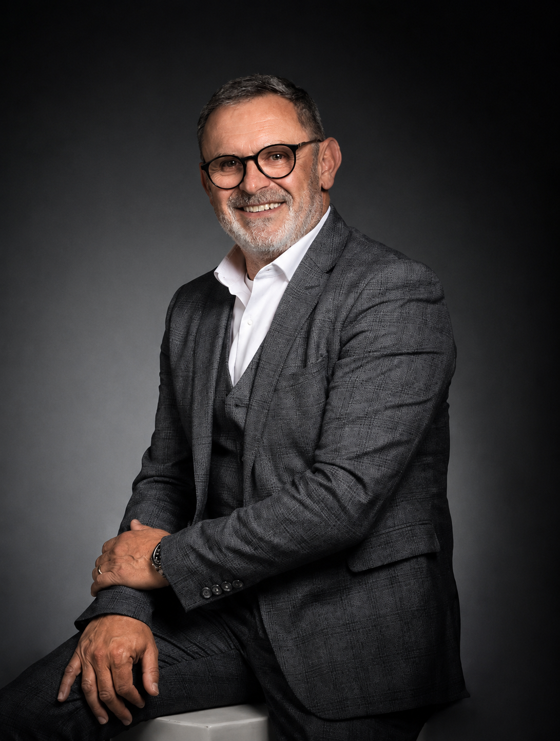 Un homme en costume et lunettes est assis sur un tabouret sur une photo en noir et blanc.