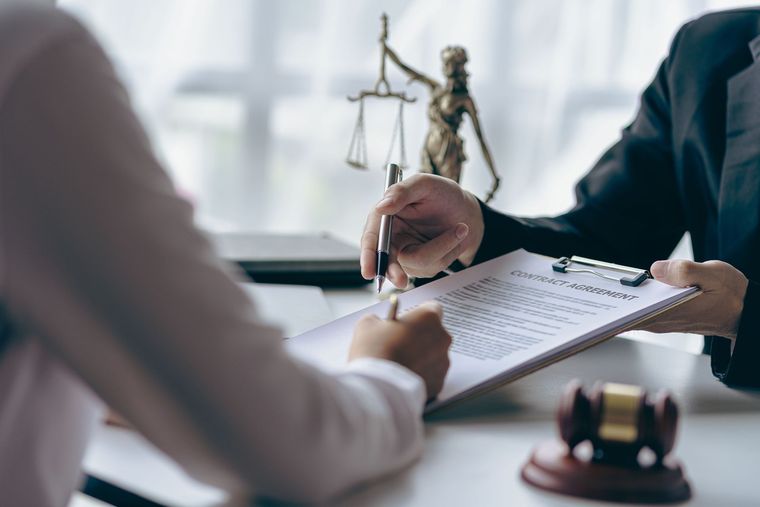 Un abogado revisa documentos en un escritorio con una estatua de la balanza de la justicia y un mazo al fondo.