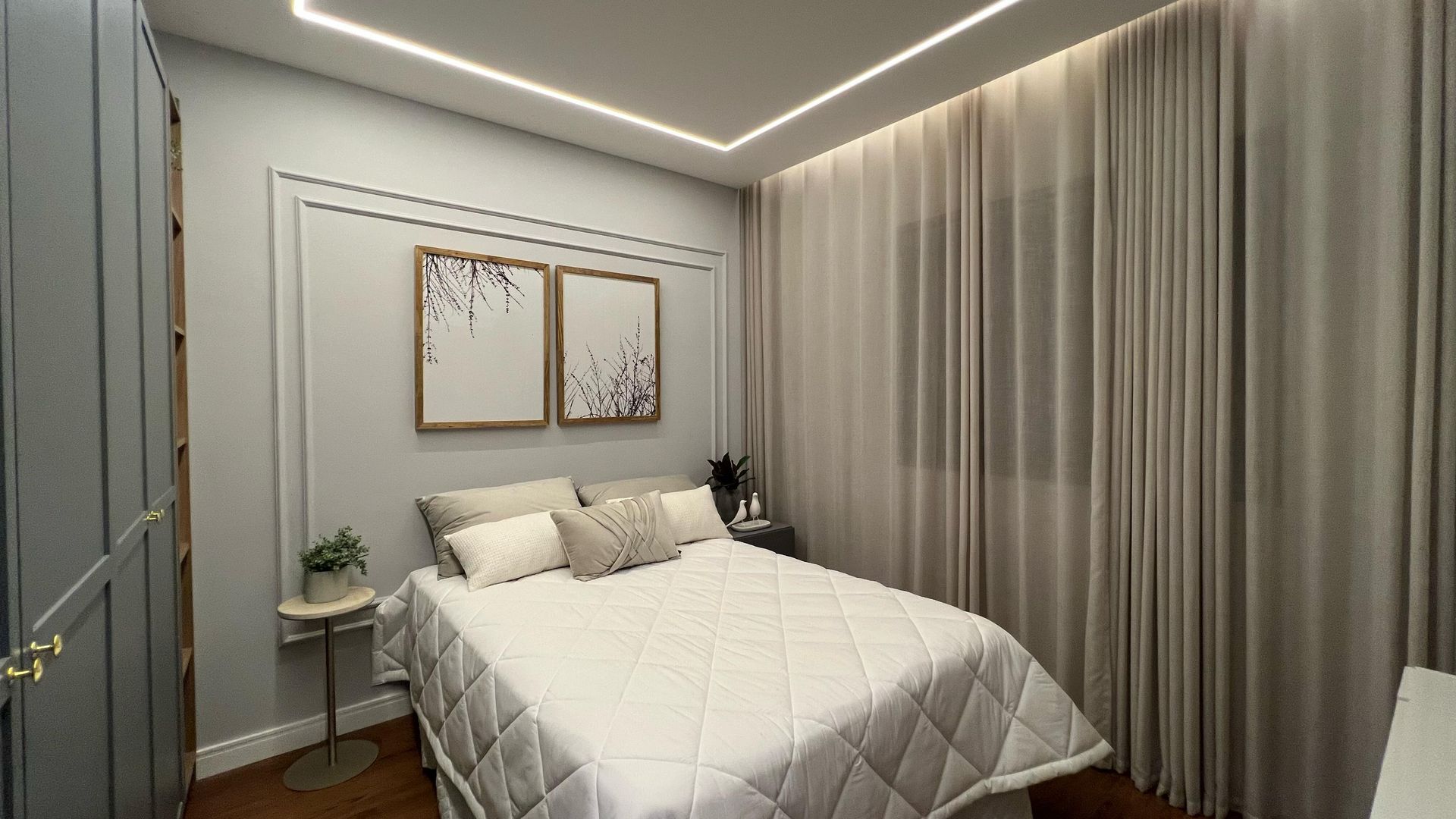 Quarto com cama, obras de arte, paredes cinza, cortinas creme e armário.