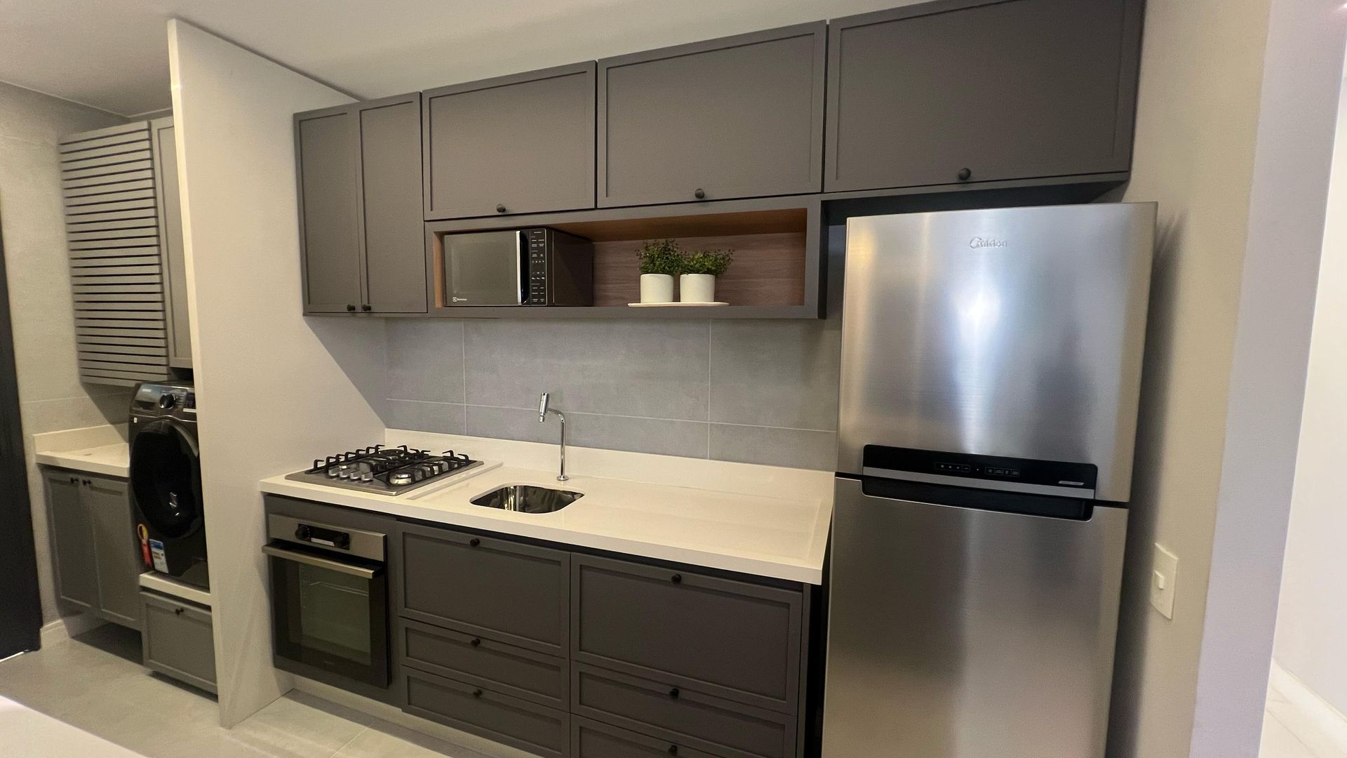 Armários de cozinha cinza com geladeira de aço inoxidável e fogão a gás pequeno.