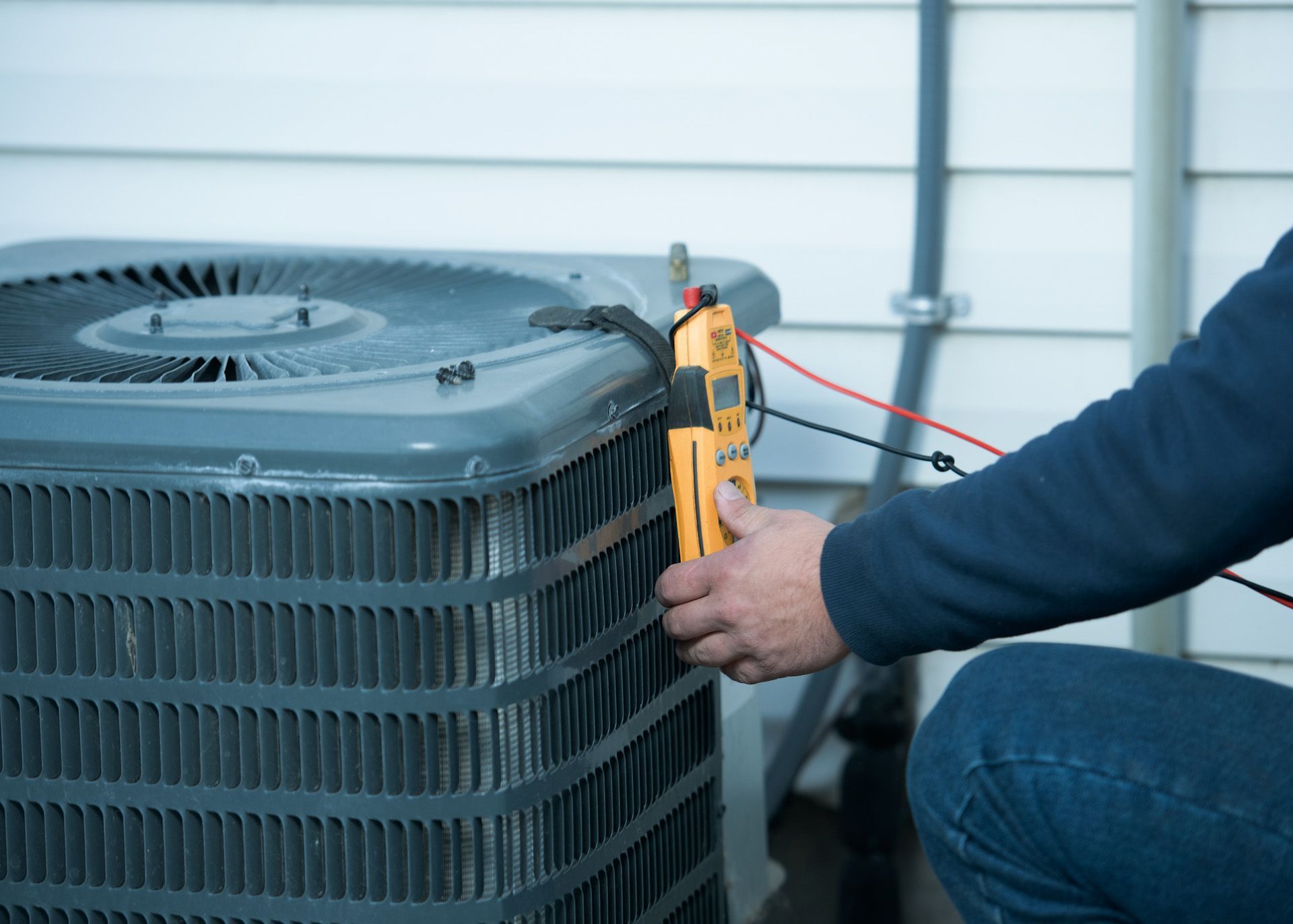 A man is working on an air conditioner outside of a house.