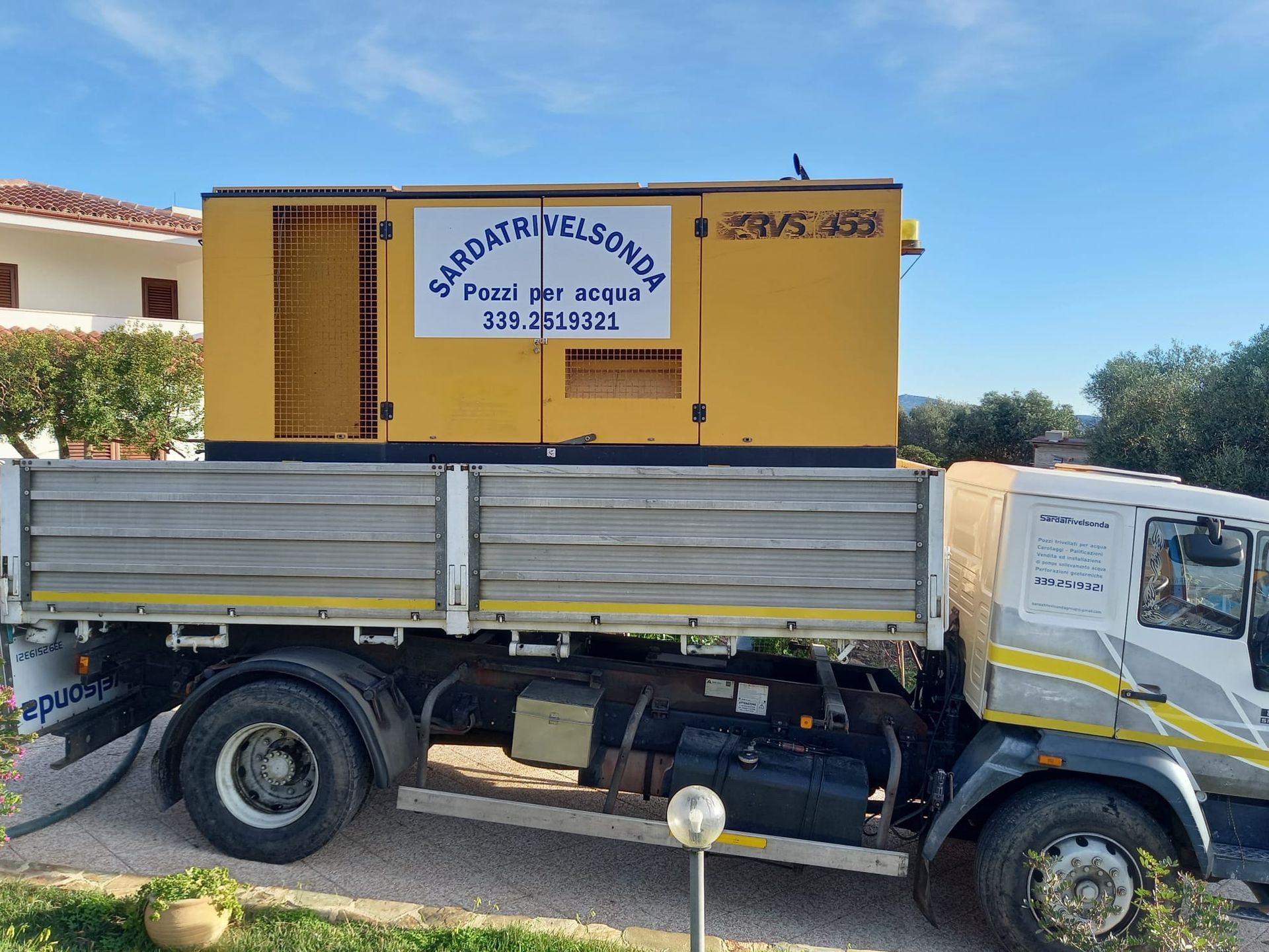 Generatore giallo sul cassone di un camion con testo, sullo sfondo cielo e un edificio Sarda Trivelsonda Group Olbia Loiri Porto San Paolo - Loiri (SS)