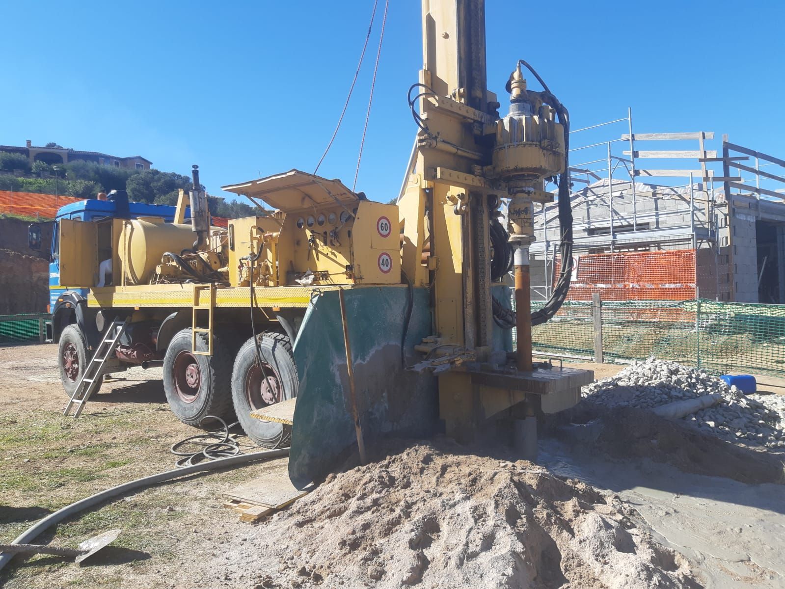 Una piattaforma di perforazione gialla in un cantiere edile, vicino a un cumulo di terra. Il cielo è azzurro e luminoso Sarda Trivelsonda Group Olbia Loiri Porto San Paolo - Loiri (SS)