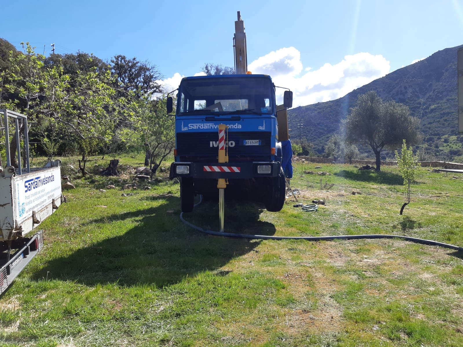Camion perforatore blu sull'erba in un campo, con una montagna sullo sfondo Sarda Trivelsonda Group Olbia Loiri Porto San Paolo - Loiri (SS)