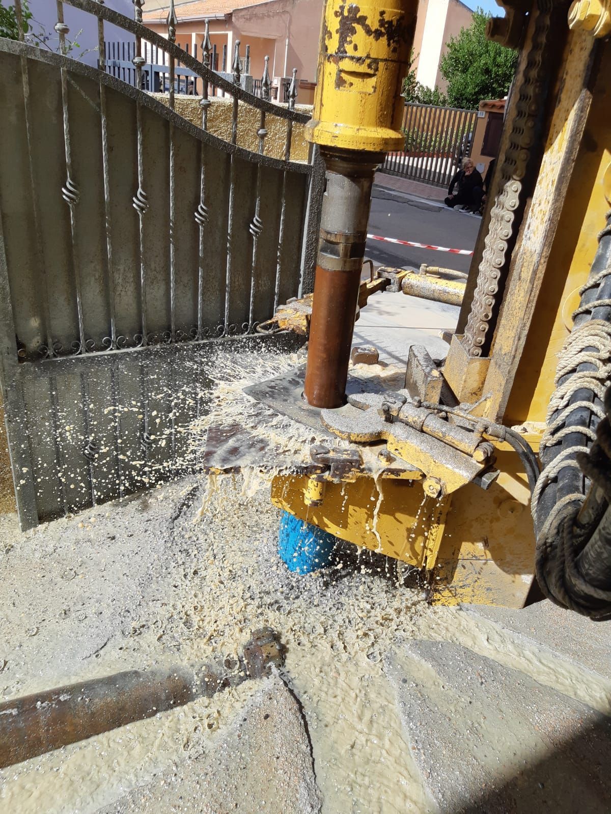 Macchina edile gialla che perfora il cemento vicino a un cancello metallico per la creazione di un pozzo artesiano Sarda Trivelsonda Group Olbia Loiri Porto San Paolo - Loiri (SS)