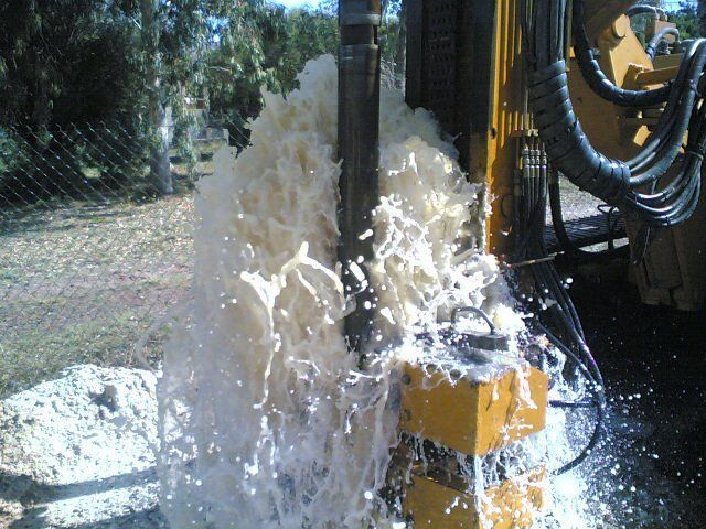 L'acqua sgorga da un tubo collegato a un'attrezzatura di perforazione gialla all'aperto, vicino a una recinzione e ad alcuni alberi Sarda Trivelsonda Group Olbia Loiri Porto San Paolo - Loiri (SS)