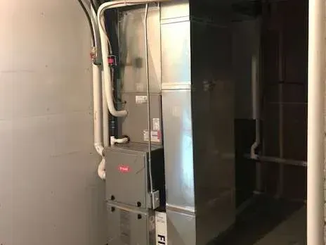 Furnace and ductwork in a basement corner. Silver metal against gray walls, white pipes.