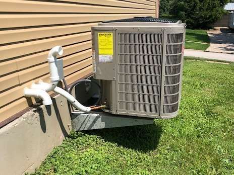 An air conditioning unit mounted on a concrete base next to a building with siding.