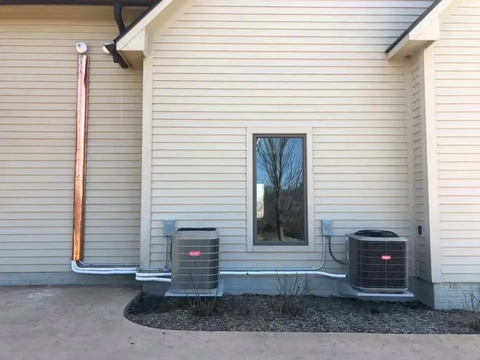 Two HVAC units and a window on the side of a beige building.