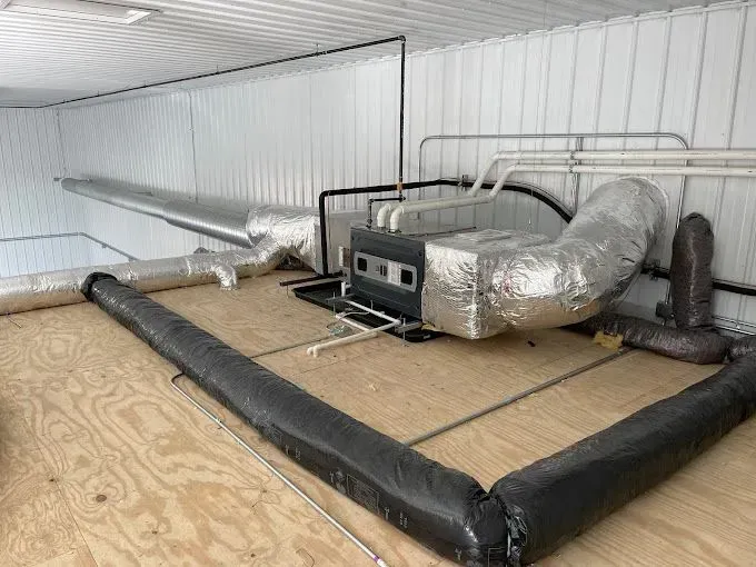 HVAC system installed in a room with wood flooring, foil-wrapped ductwork, and black insulated piping.