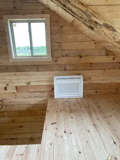 Loft interior with window, air conditioner, and wood paneling.