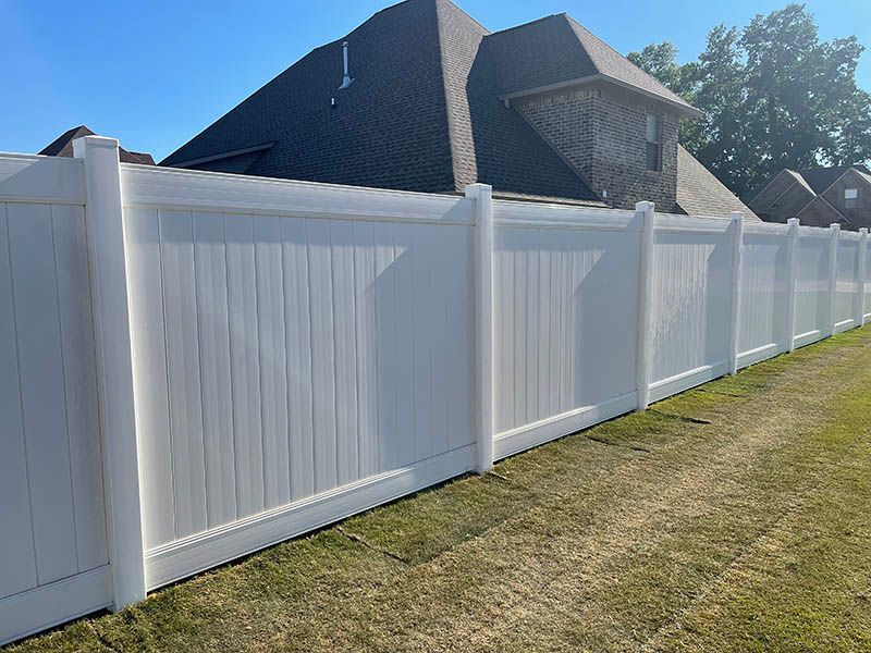 A white fence surrounds a grassy yard in front of a house.
