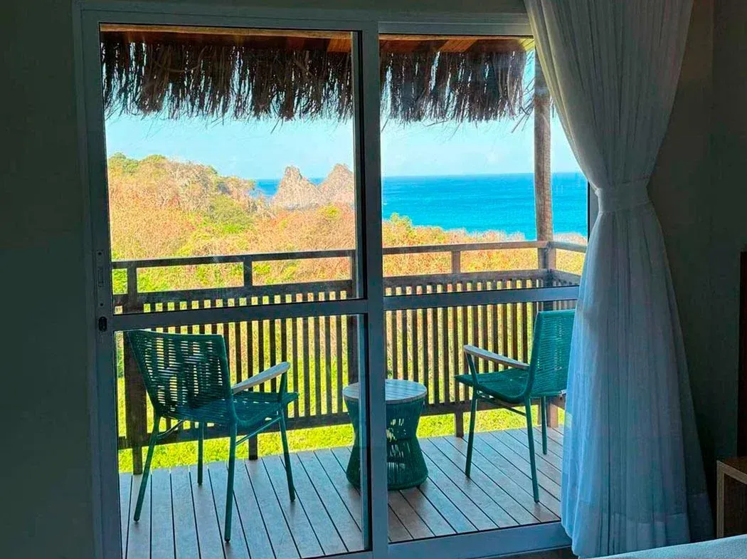 Um quarto com porta de correr de vidro que dá acesso a uma varanda com vista para o mar.