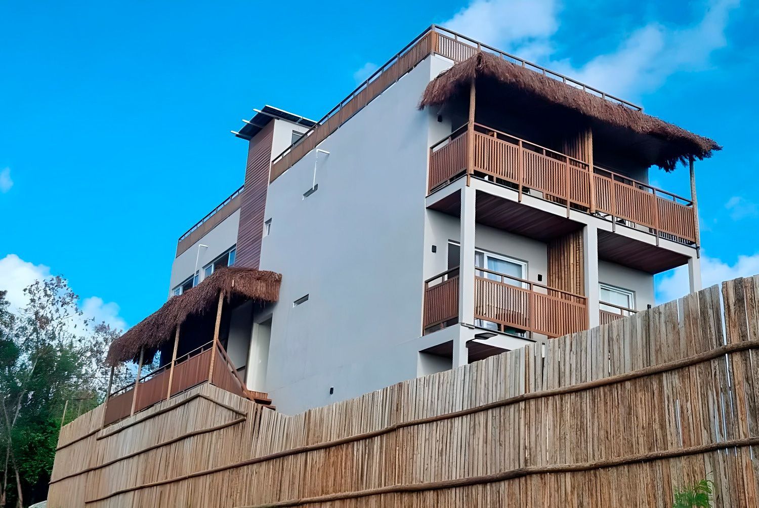 Um grande edifício branco com telhado de palha fica atrás de uma cerca de madeira.