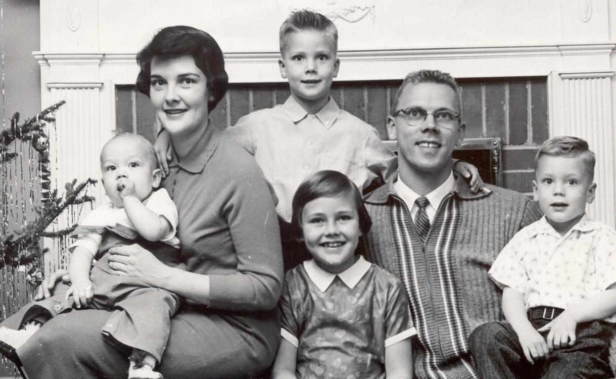 A family of six, smiling, poses in front of a fireplace.