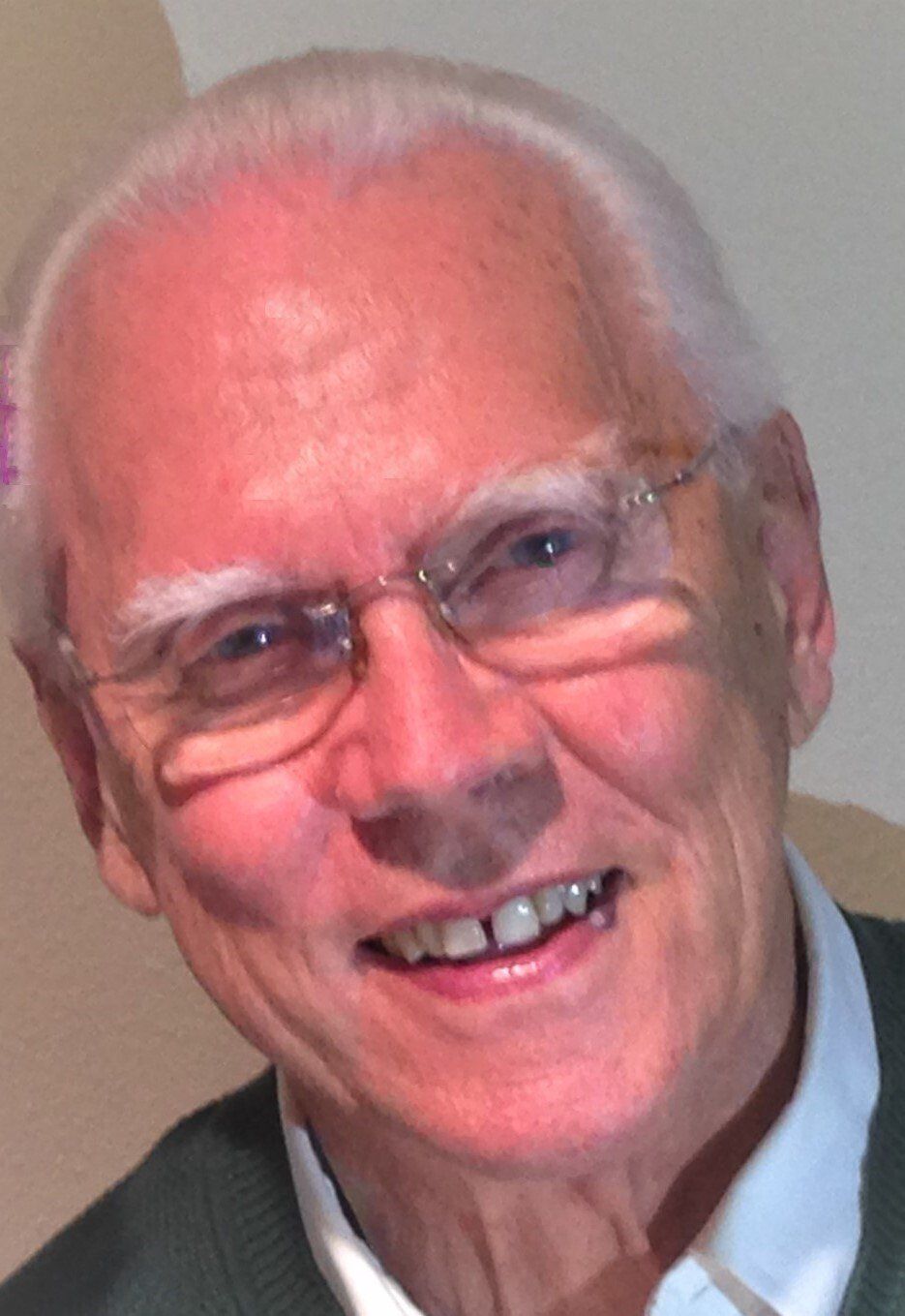 Smiling elderly man with glasses, white hair, wearing a green shirt.