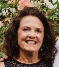 Woman with dark curly hair smiles in front of flowers.