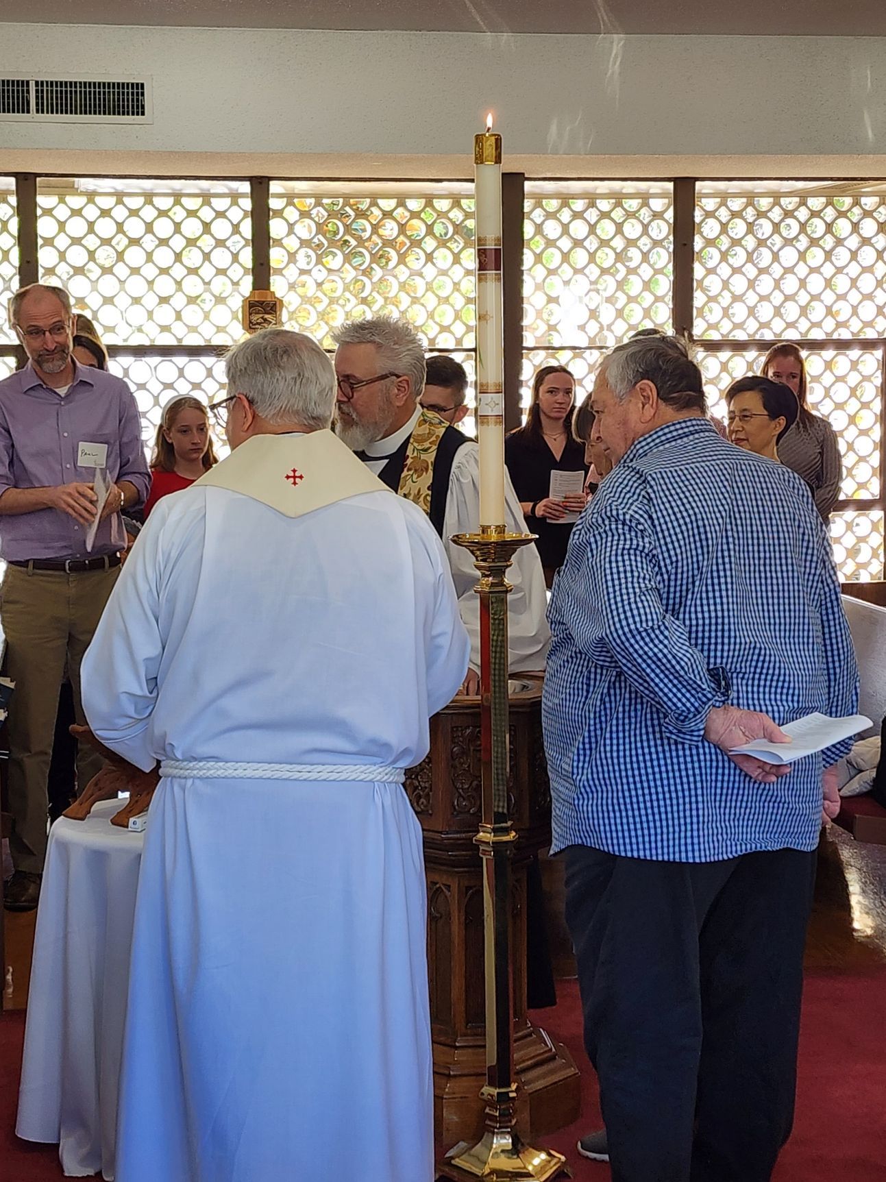 People gathered near a church altar with a lit candle, possibly a baptism or religious ceremony.