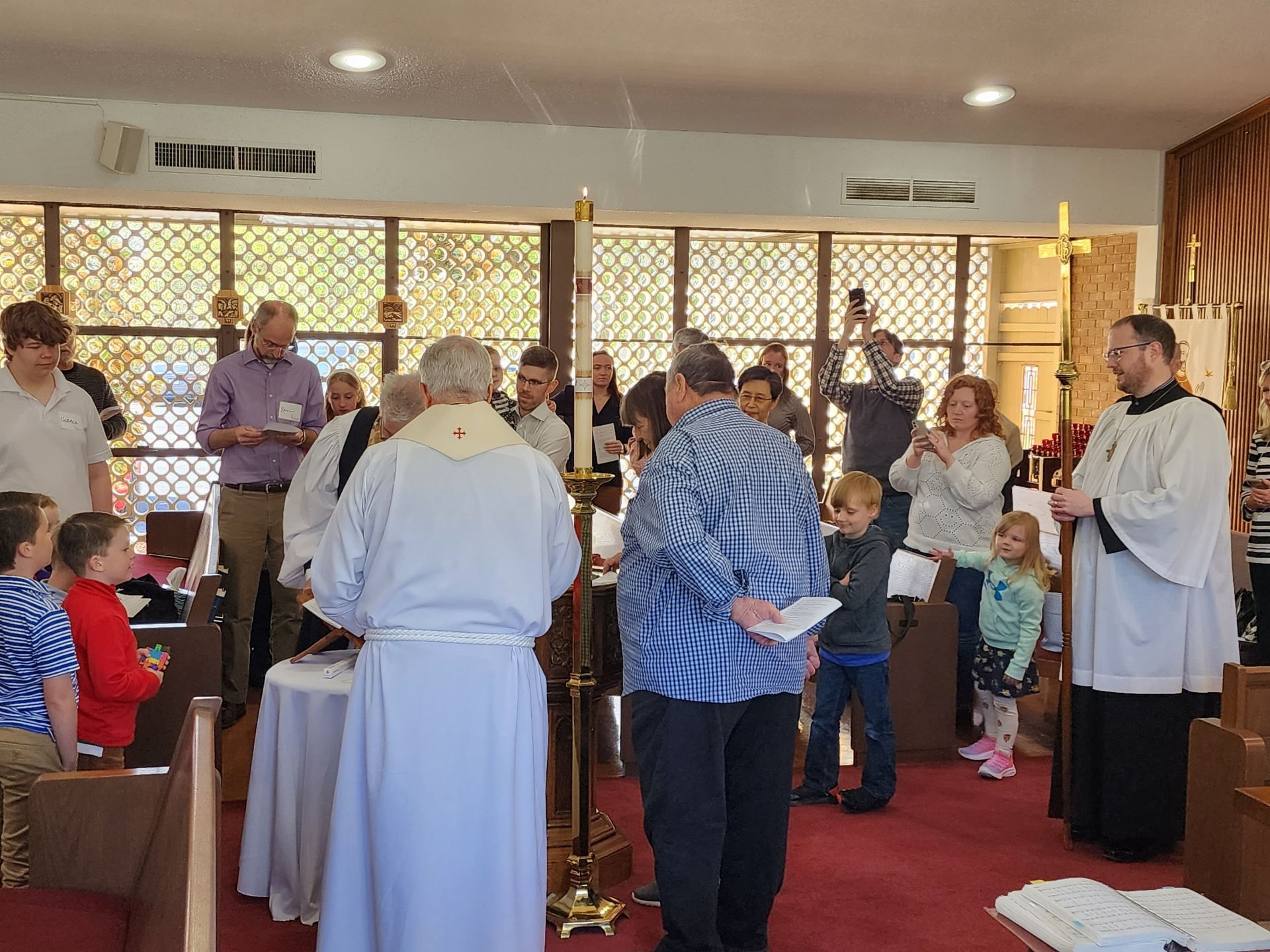 Church service: priest, people, baptism ceremony in progress, sunlight streaming through windows.